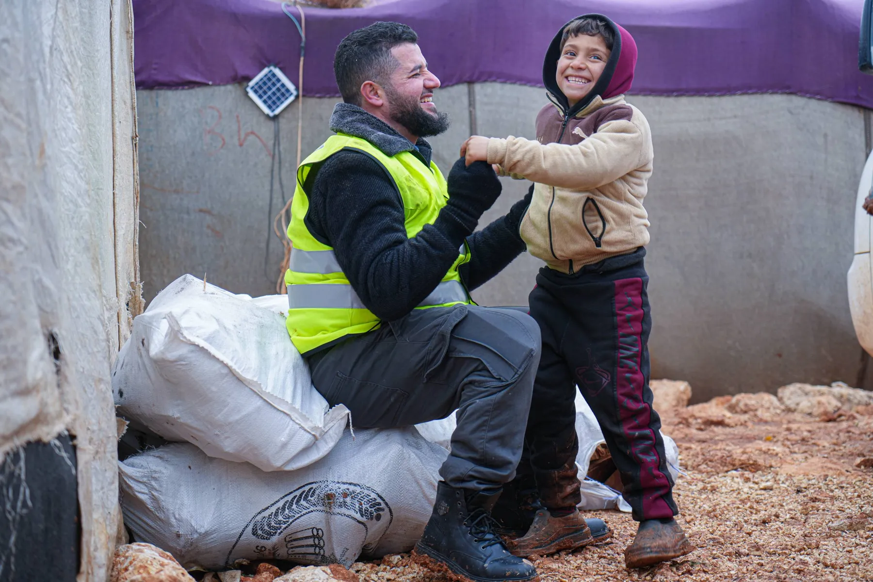 Aid worker and a smiling boy beside sacks of winter supplies