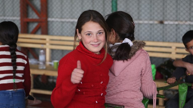 Smiling girl giving a thumbs up beside a friend