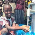 Smiling girl washing her hands at a Uganda water well