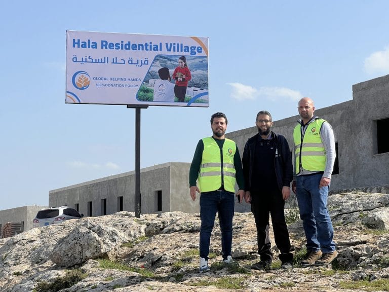 Three team members in front of the Hala Residential Village sign