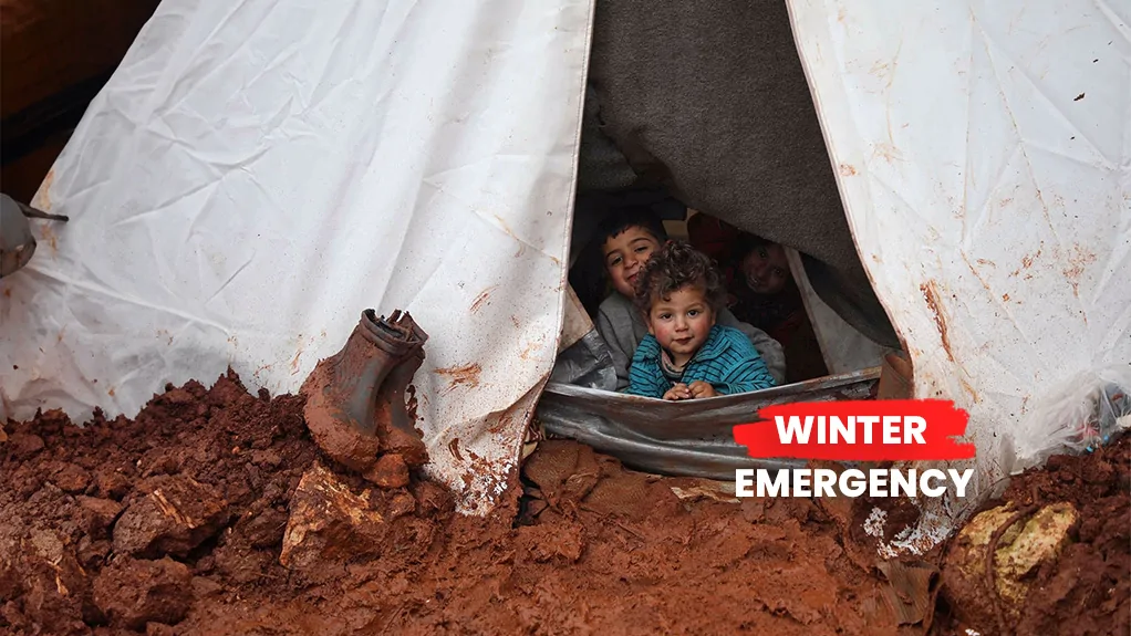 Young children sheltering in a tent pitched in mud, Winter Emergency