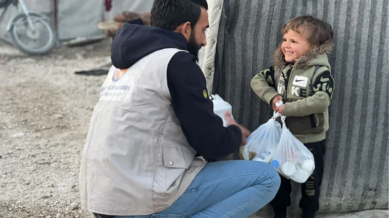 Aid worker giving bags of supplies to a young boy in a camp