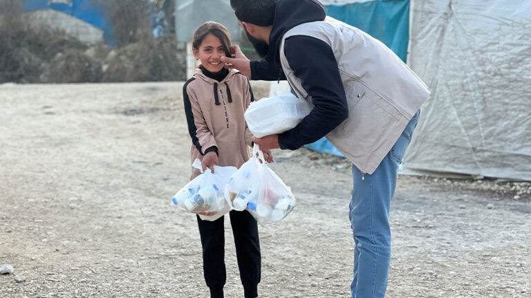 Aid worker giving bags of supplies to a girl in a camp