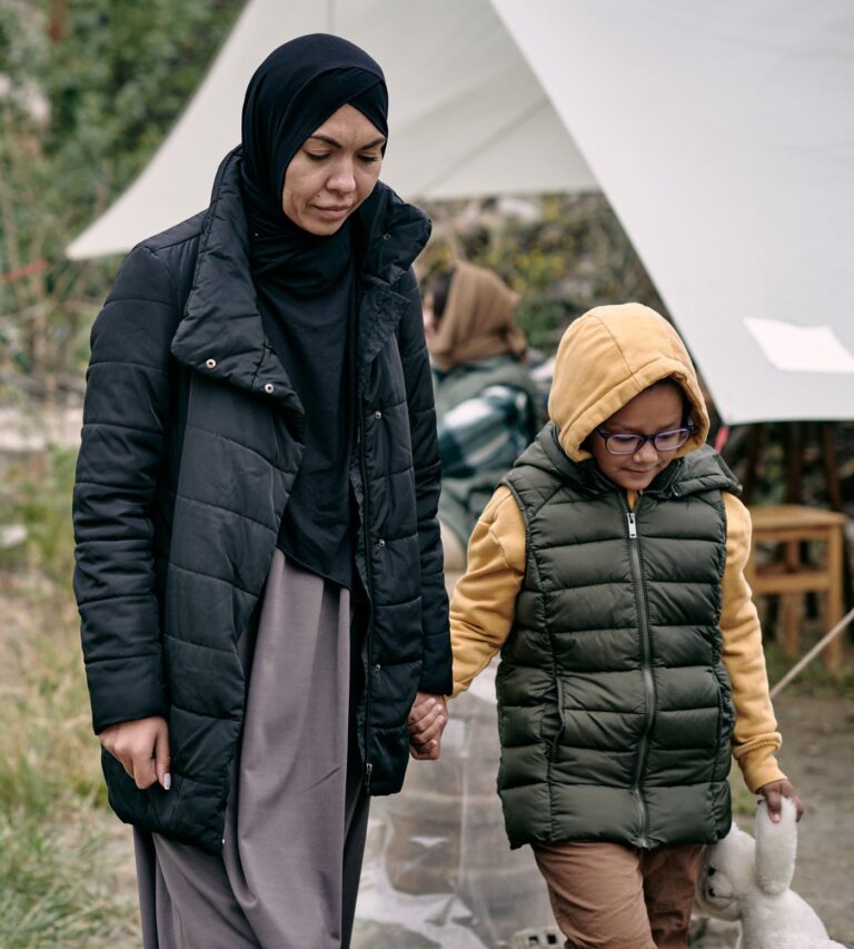 A mother and her daughter walk hand in hand through a camp of tents