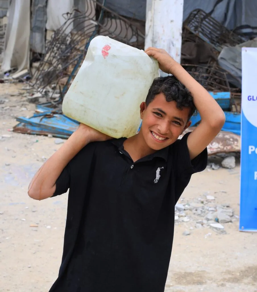 Smiling boy carrying clean water from the Global Helping Hands water tanker in Palestine