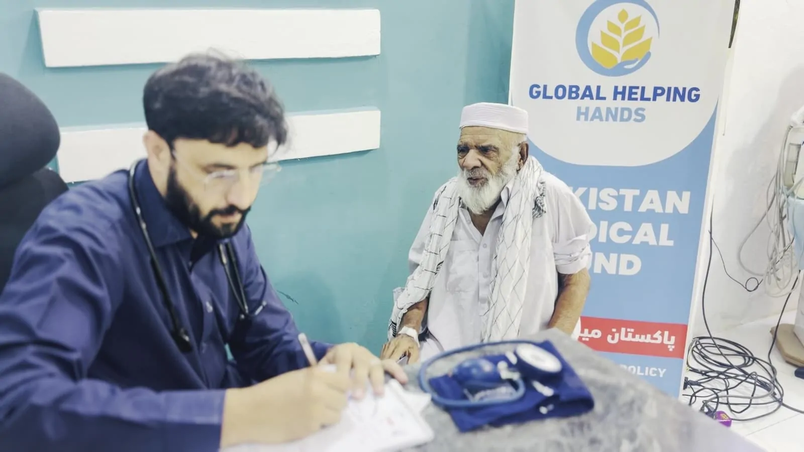 Doctor writing up an elderly patient's check-up at the Pakistan Medical Fund clinic